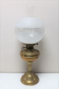 An antique brass oil lamp with glass chimney and shade