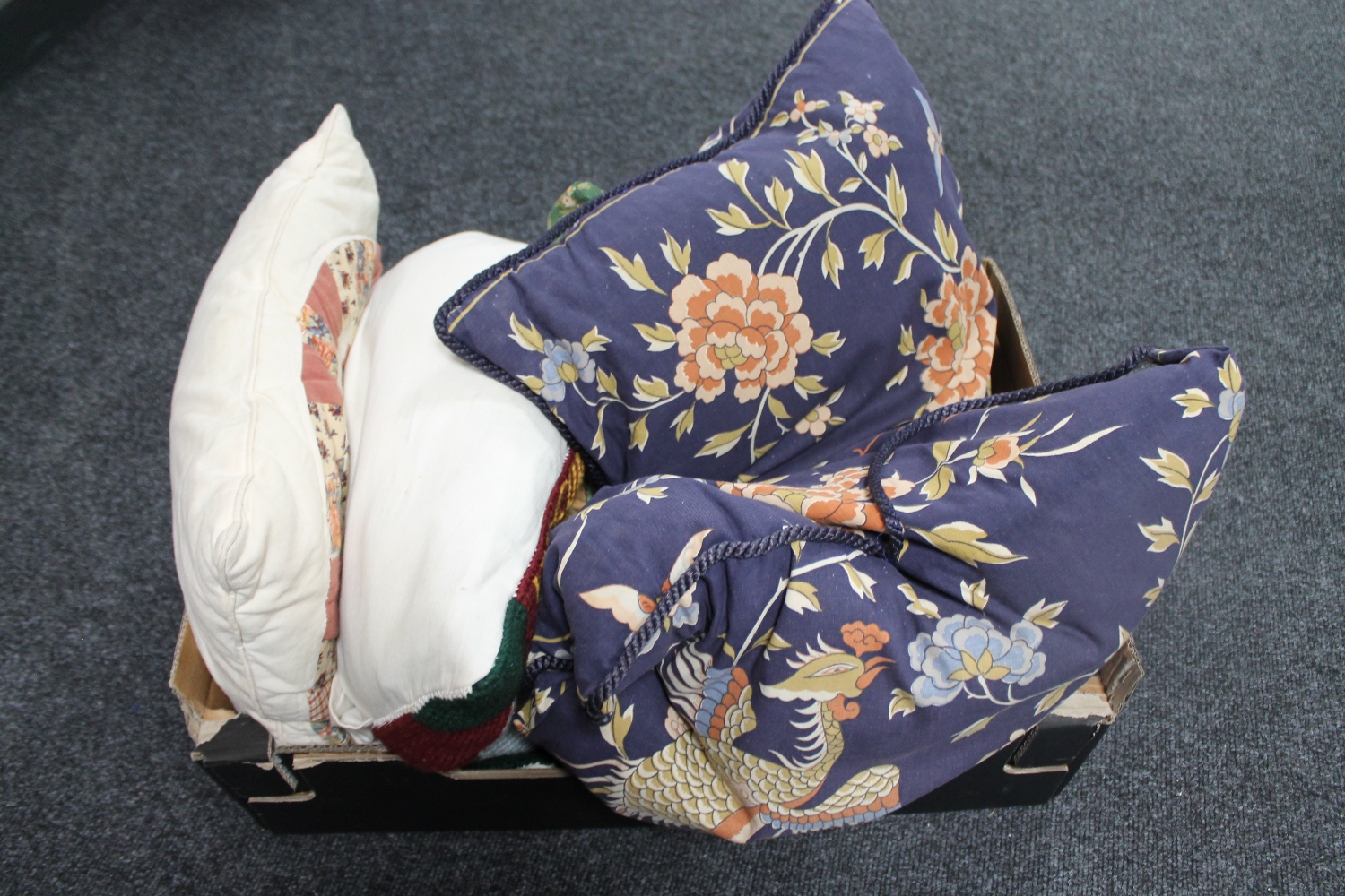 A box containing a tapestry cushion together with two patchwork cushions and two further blue