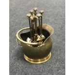 An antique brass coal bucket and four piece companion set on stand