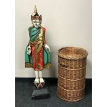 A carved wooden painted figure of an eastern deity together with a circular wicker laundry basket