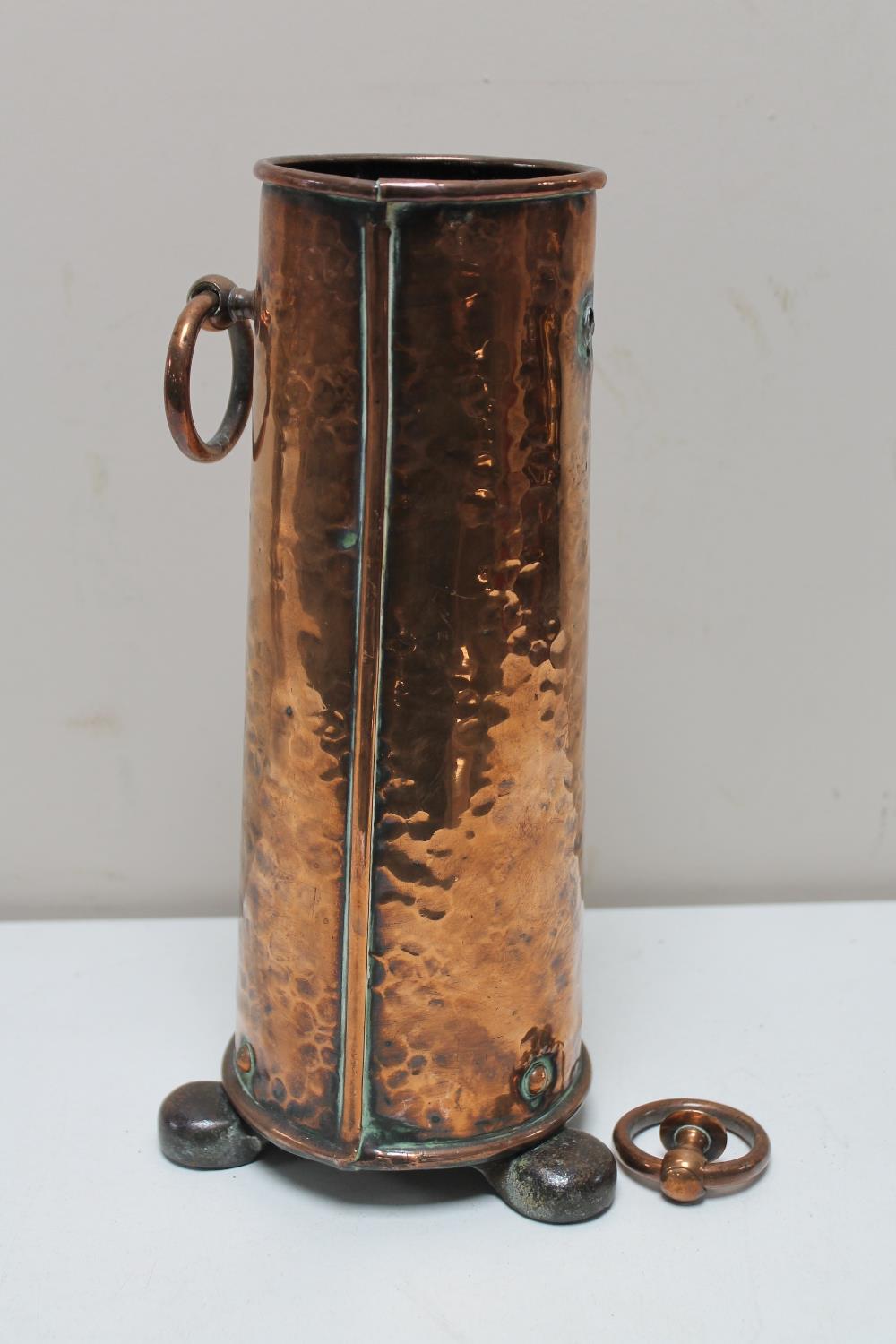 An antique hammered copper vase on metal feet