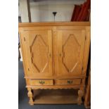 A blonde oak double door cabinet on stand