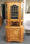 A blonde oak corner cabinet with stained leaded glass panels