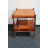 An inlaid yew wood two tier occasional table on brass castors fitted a drawer and pull out slide