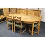 A circular blonde oak extending table with three leaves and six ladder back chairs