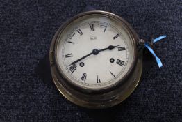 A circular brass cased Sui ship's clock with key mounted on a Bakelite board