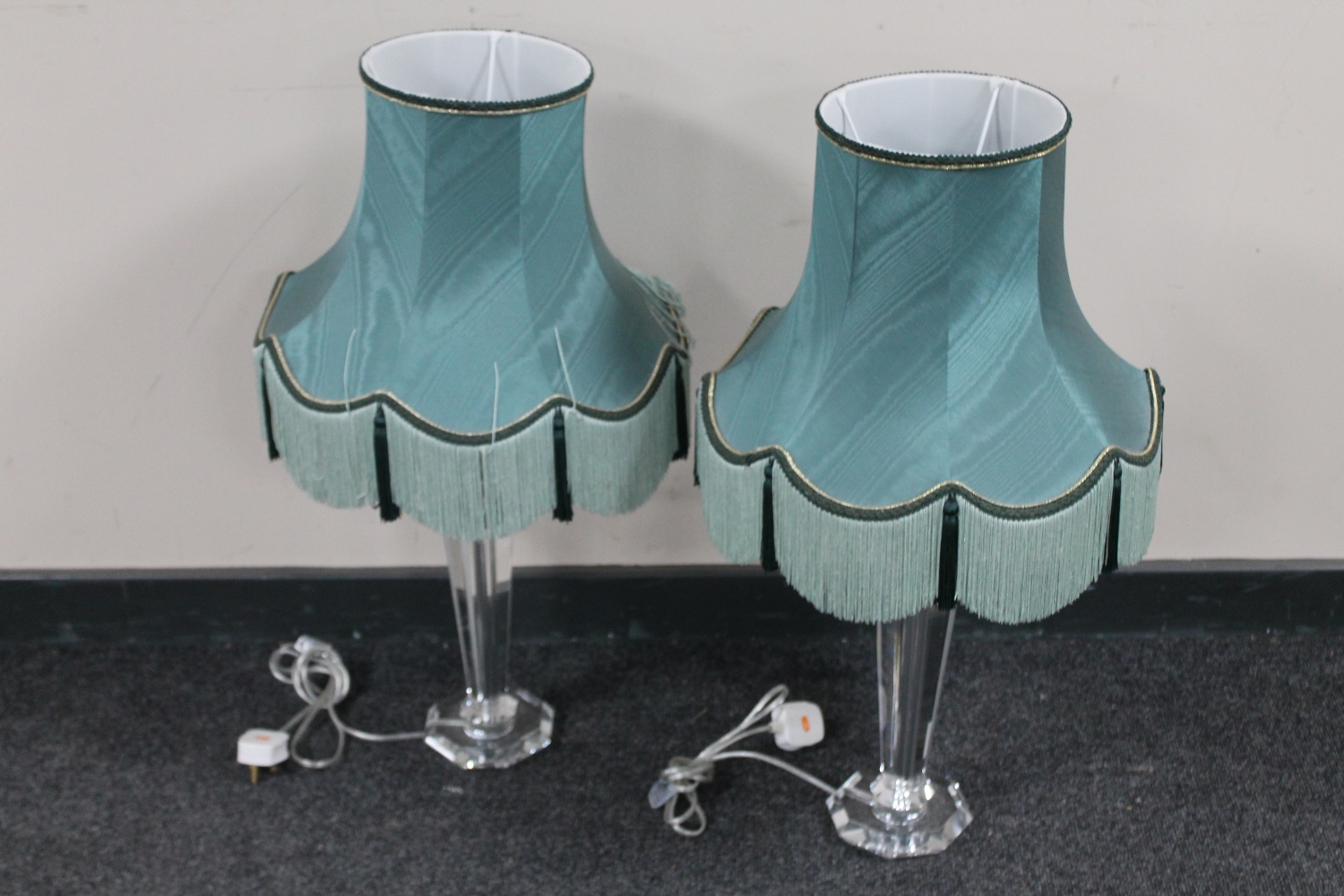 A pair of clear perspex table lamps with green tasselled shades