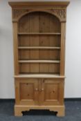 A set of carved pine open bookshelves fitted double door cupboards beneath,