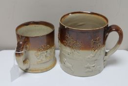 Two antique stoneware mugs depicting hunting and farming scenes.