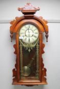 An early 20th century stained pine wall clock with enamelled dial and pendulum