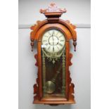 An early 20th century stained pine wall clock with enamelled dial and pendulum