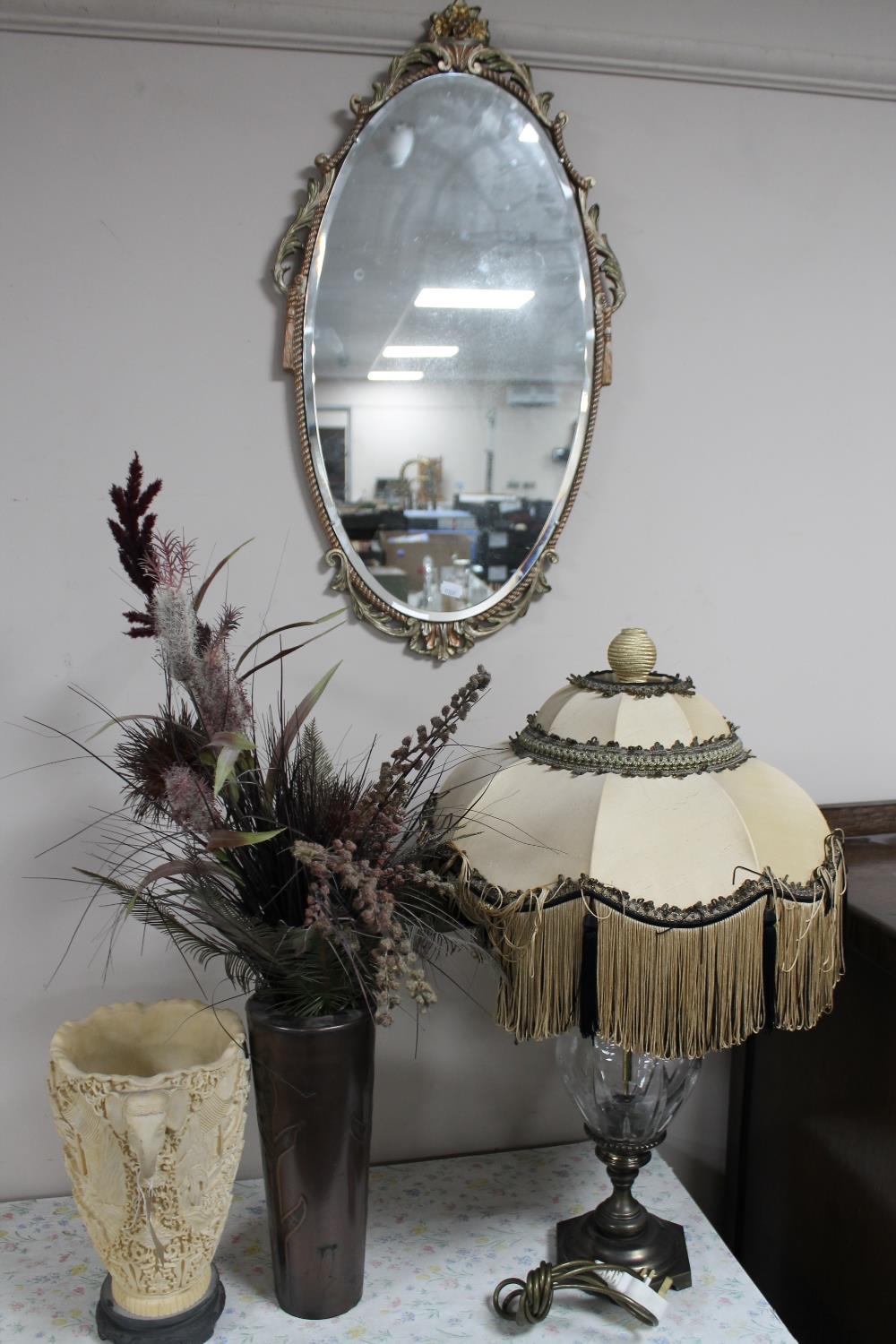 An oval gilt framed bevelled edge wall mirror together with a metal and glass table lamp with shade,