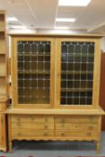 A blond oak double door cabinet with leaded glass doors fitted with six drawers