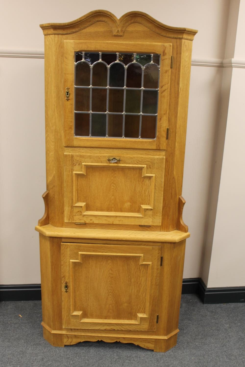 A blond oak corner cabinet with stained leaded glass panel