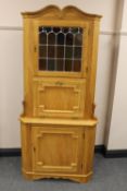 A blond oak corner cabinet with stained leaded glass panel