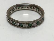 An 18ct white gold diamond and emerald full eternity ring, size N/O.