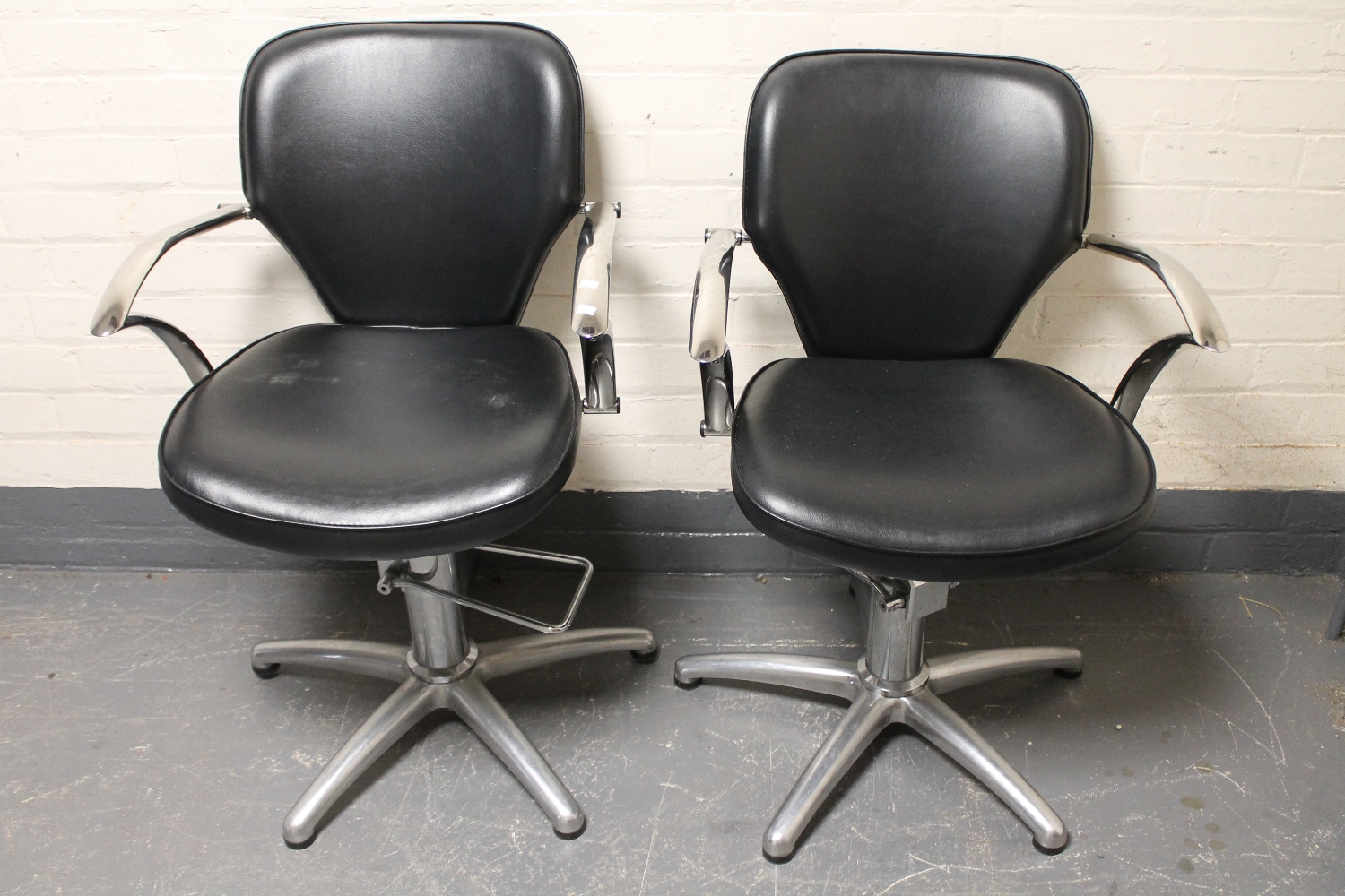 A pair of black vinyl and metal hydraulic barber's chairs