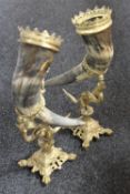 A pair of cow horns with brass mounts on ornate brass stands
