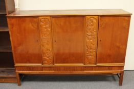 A stained beech triple door sideboard with two carved panels with three drawers beneath