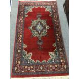 A fringed Persian rug of geometric design on red ground