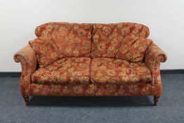 A two seater settee upholstered in a red floral fabric together with two scatter cushions