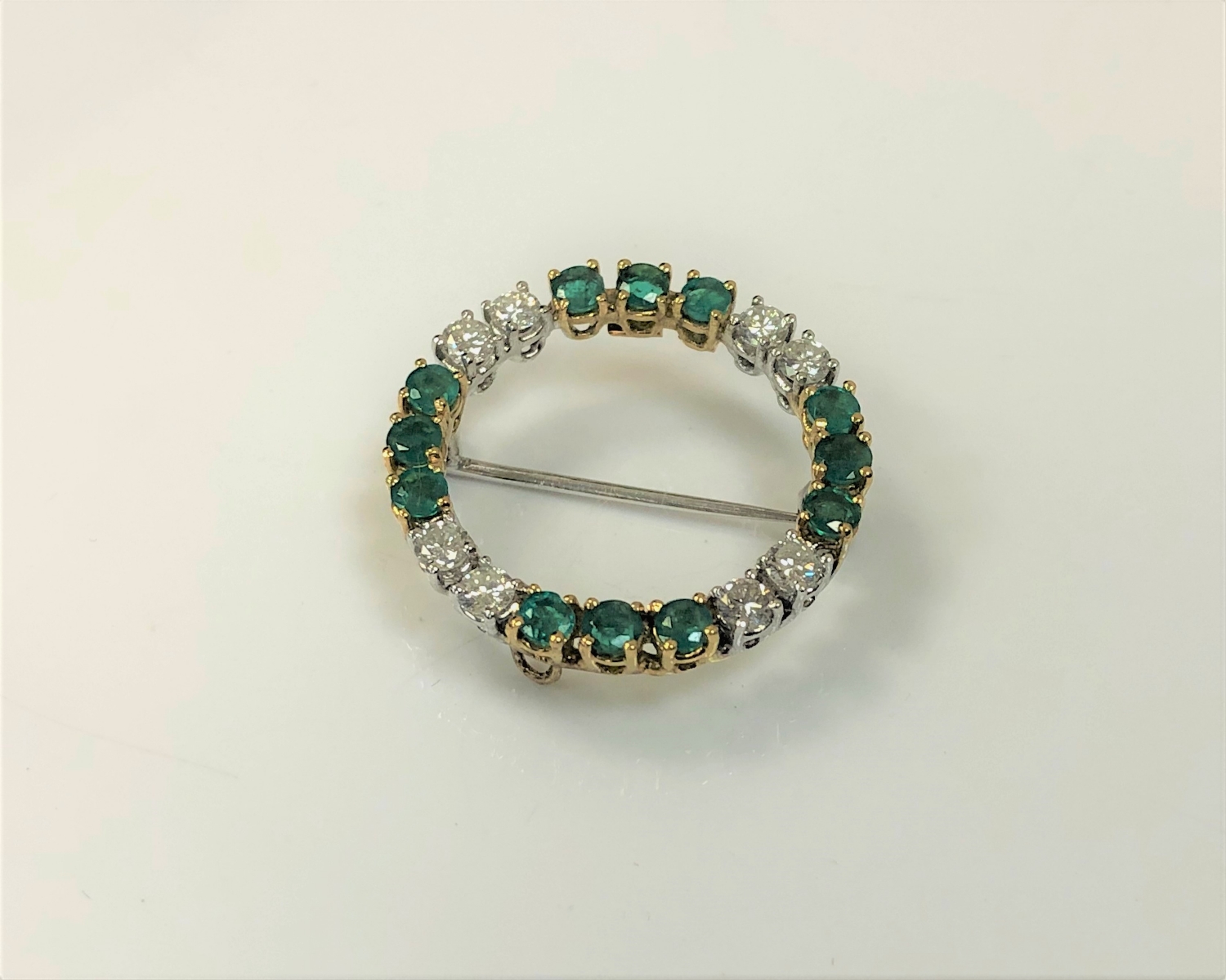 An 18ct gold diamond and emerald circular brooch, approximately 1.5ct, 5.2g.