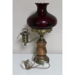 A continental wood and brass oil lamp with chimney and red glass shade (wired)