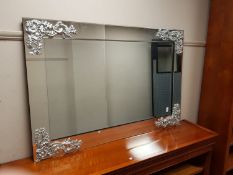 A contemporary silver scroll and bevelled glass overmantel mirror,