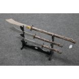Three graduated Chinese style twin handled swords on a wooden stand