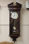 A contemporary mahogany wall clock with two weights and pendulum