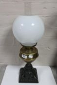 An antique brass oil lamp with glass chimney and shade on cast iron base