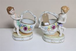 A pair of continental porcelain cherub baskets with flower encrusted decoration