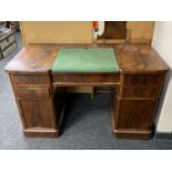 An antique mahogany twin pedestal writing desk fitted with five drawers and cupboards with green