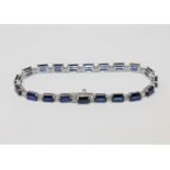 A 14ct white gold sapphire and diamond bracelet, the twenty emerald-cut sapphires weighing 12.