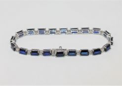 A 14ct white gold sapphire and diamond bracelet, the twenty emerald-cut sapphires weighing 12.