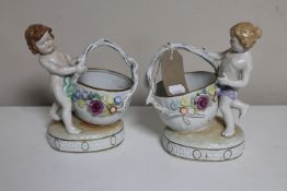 A pair of continental porcelain cherub baskets with flower encrusted decoration