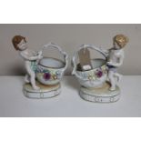 A pair of continental porcelain cherub baskets with flower encrusted decoration