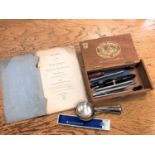 A cigar box containing pens including Parker, plated spoons, pen knives,