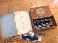 A cigar box containing pens including Parker, plated spoons, pen knives,