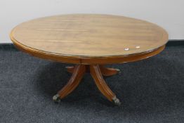 An inlaid yew wood oval pedestal coffee table with glass top