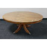 An inlaid yew wood oval pedestal coffee table with glass top