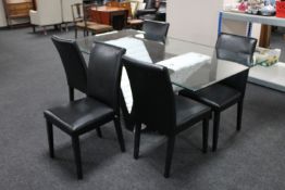 A glass topped dining table and five black vinyl chairs