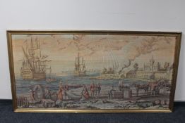 A gilt framed tapestry of boats landing in a harbour