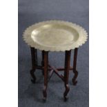 An ornate brass topped table on a folding wooden base