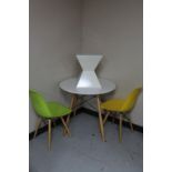 A circular contemporary dining table on wooden legs together with two plastic dining chairs on