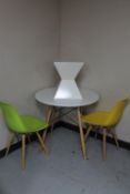 A circular contemporary dining table on wooden legs together with two plastic dining chairs on
