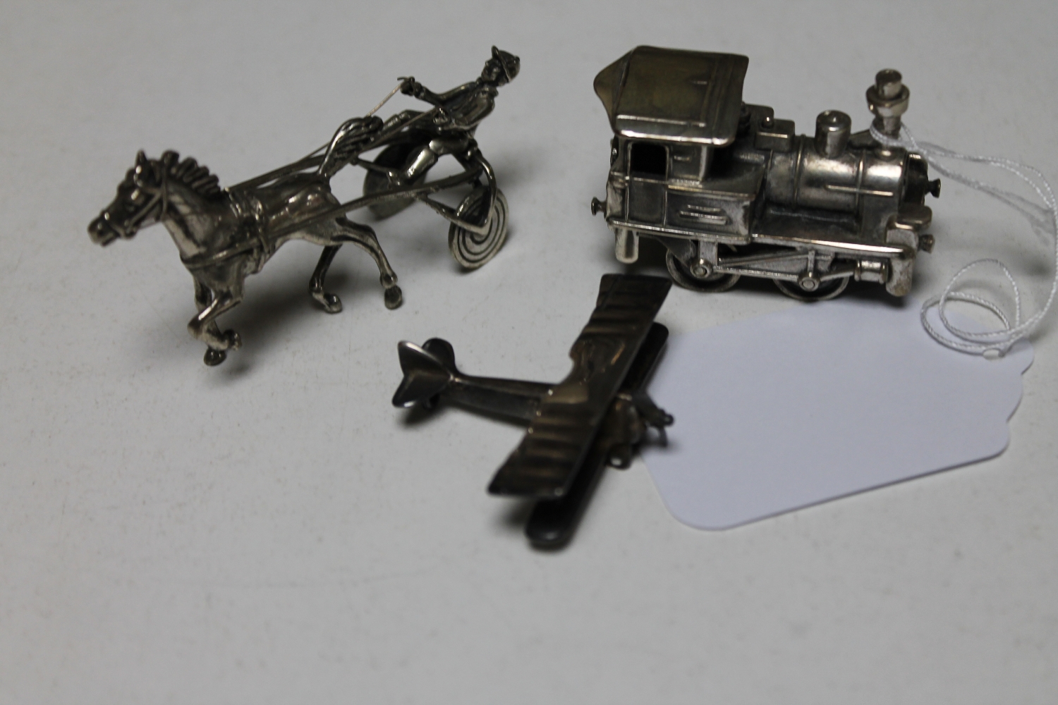 Three miniature silver models of a locomotive, a horse and trap and an aeroplane,