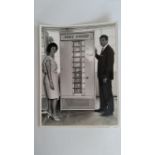 CRICKET, press photo, Australian, showing Richie Benaud & his wife inspecting a vending machine,