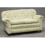 An early 20th century two-seat drop-end sofa, upholstered in a cream cord fabric, on bun feet and