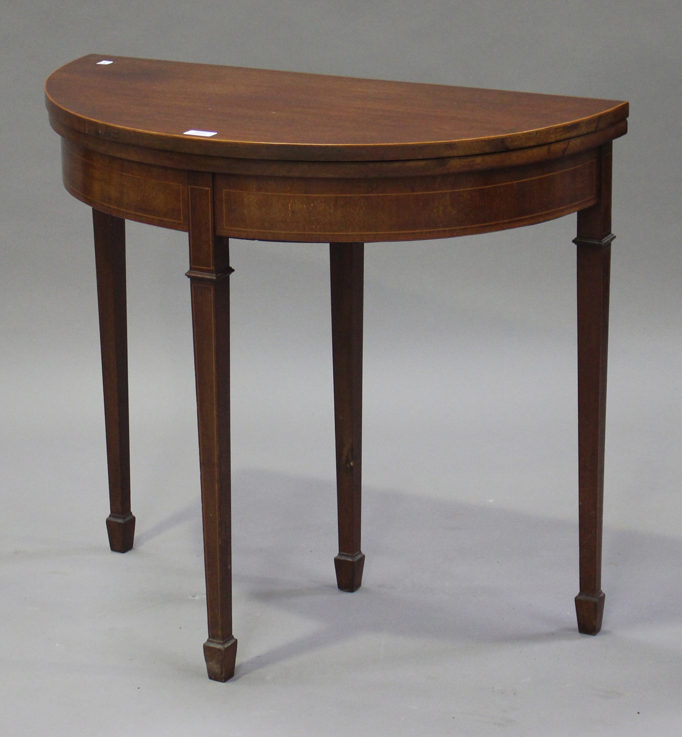 An Edwardian mahogany demi-lune fold-over card table, raised on square tapering legs, height 75cm,